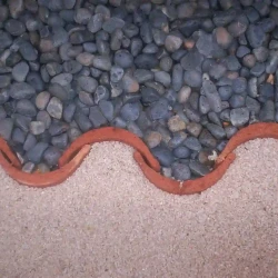 Roof tiles used on edge as edging. Border. Black pebbles and beige gravel.