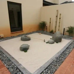 Driveway & entrance. Zen dry raked gravel Japanese garden, grey rocks, beige gravel, concrete border, black pebbles, 3 upright bamboo poles, wooden zen rake.
