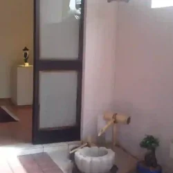 Tiny entrance garden with solid granite lotus bowl Japanese water basin (tsukubai), bamboo water feature (kakehi), bamboo ladle and rest, bonsai on rock, gravel, pebbles.