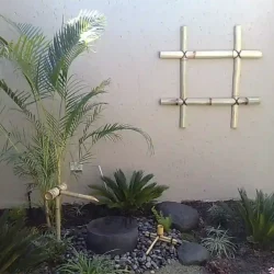 Modern tropical Japanese style garden, Japanese water pot (tsukubai) with bamboo water feature (kakehi) and bamboo ladle and rest, surrounded by pebbles, palm, cycas revoluta. Split bamboo wall cladding. Bamboo cross hatch wall ornament.