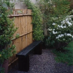 Rustic sleeper wood bench with bamboo screen behind, white azalea, gravel.