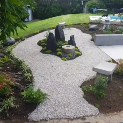 Three monolith rocks and Japanese water basin (tsukubai) set into mossy mound, surrounded by beige gravel in centre of meditation garden. Small curved Zen benches.