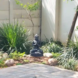 Corner garden bed around swimming pool with small Buddha ornament