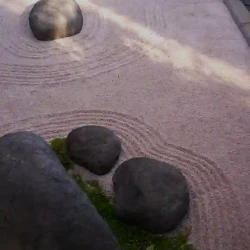 Dry raked Japanese Zen garden comprising only rocks, gravel and moss with a black pebble border