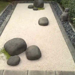 Dry raked Japanese Zen garden comprising only rocks, gravel and moss with a black pebble border