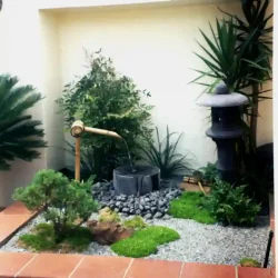 Tiny Japanese garden in raised planter by entrance with Japanese water basin, Japanese lantern and shaped tree with mosses, surrounded by gravel.