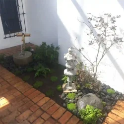 Tiny entrance garden with Japanese water basin (tsukubai) and bamboo water feature (kakehi), small pedestal style Japanese lantern, Japanese Maple tree, black pebbles, rocks, ferns, mossy ground covers.