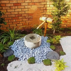 Japanese water basin (tsukubai) with bamboo water feature (kakehi). Black pebbles. Gravel path.
