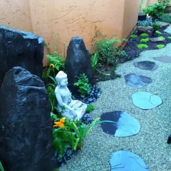 Small Buddha with three monolith grey rocks. Grey gravel path with black slate steppingstones.