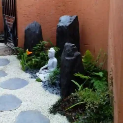 Small Buddha with three monolith grey rocks. Grey gravel path with black slate steppingstones.